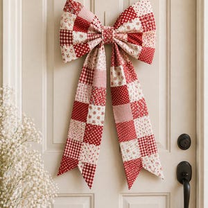 May include: A large, decorative bow made of patchwork fabric, featuring red and white patterns including polka dots, floral prints, and gingham. The bow is hanging on a white door, with a black door handle and lock visible.