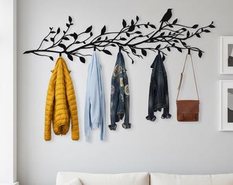 Puede incluir: Un perchero de pared de metal negro con forma de rama de árbol con un pájaro. El perchero sostiene una chaqueta acolchada amarilla, un suéter azul claro, una chaqueta vaquera, una chaqueta vaquera oscura y un bolso de cuero marrón.