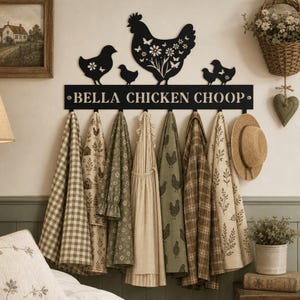 Può includere: Un appendiabiti da parete in metallo nero con la sagoma di una grande gallina, pulcini e intagli floreali. Il testo BELLA CHICKEN CHOOP è stampato sul davanti. Otto ganci sostengono vari tessuti a fantasia, grembiuli e un cappello di paglia.
