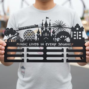 May include: Black metal wall art featuring a silhouette of a castle, train, and other theme park icons. The text "MAGIC LIVES IN EVERY JOURNEY" is included. The art has three horizontal bars below the design.