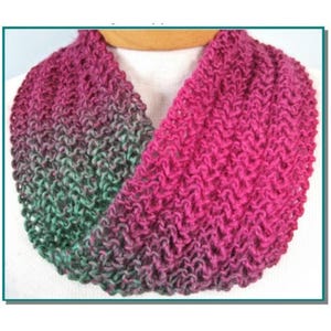 May include: A knitted infinity scarf in shades of pink and green. The scarf is a continuous loop, with a textured stitch pattern. The colors transition from pink to green, creating a gradient effect. The scarf is likely made of soft yarn.