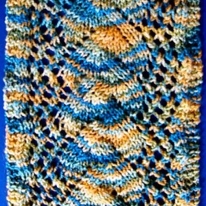Könnte beinhalten: Nahaufnahme eines gestrickten Schals mit einem blauen, grünen und orangen Farbmuster. Der Schal ist mit einer Lochmasche gestrickt und hat ein diagonales Muster.