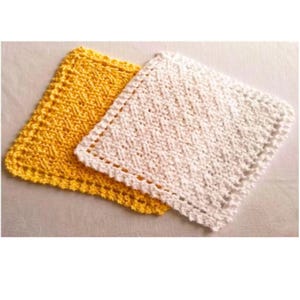 May include: Two handmade crochet washcloths. One is bright yellow, the other is white. Both have a textured pattern and a decorative border. These square cloths are likely used for cleaning or as decorative items.