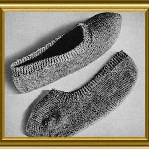 May include: A pair of grey knitted slippers featuring a textured stitch pattern, a rounded toe, and a ribbed collar. The slippers are captured in a black and white photograph, showcasing the detailed knit construction and the soft, flexible shape of the footwear.