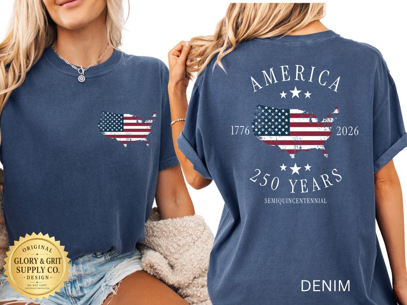 May include: Denim blue t-shirt with a distressed American flag design in the shape of the United States. The back of the shirt features the word "AMERICA", the years "1776" and "2026", and "250 YEARS SEMIQUINCENTENNIAL".