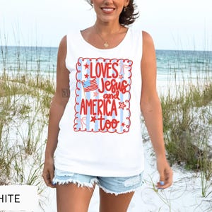 K&ouml;nnte beinhalten: Wei&szlig;es Tanktop mit dem Text "LOVES Jesus and AMERICA too" in Rot und Blau. Das Design beinhaltet eine amerikanische Flagge und Sterne. Das Tanktop ist &auml;rmellos und aus weichem Material.
