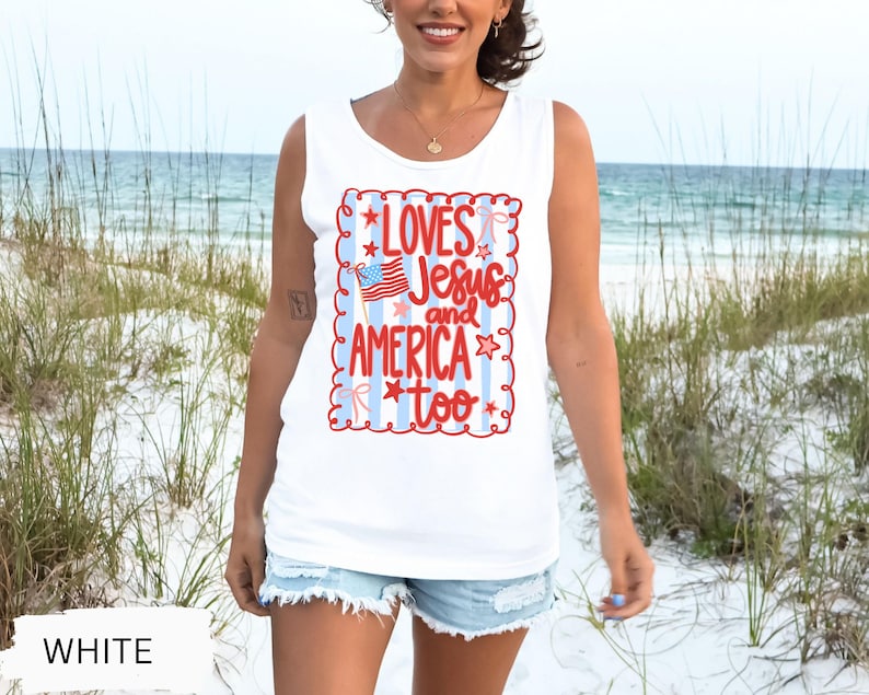 K&ouml;nnte beinhalten: Wei&szlig;es Tanktop mit dem Text "LOVES Jesus and AMERICA too" in Rot und Blau. Das Design beinhaltet eine amerikanische Flagge und Sterne. Das Tanktop ist &auml;rmellos und aus weichem Material.