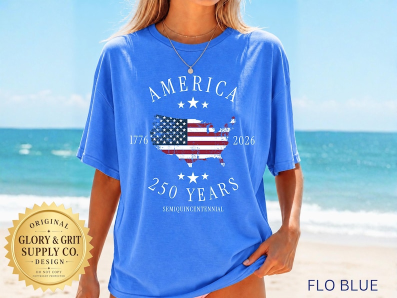 May include: A blue t-shirt with the word "AMERICA" arched across the top and the years "1776" and "2026" flanking a map of the United States with a flag design. The text "250 YEARS" is below the map, with "SEMIQUINCENTENNIAL" below that. The shirt is labeled "FLO BLUE".