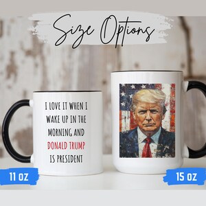 K&ouml;nnte beinhalten: Zwei wei&szlig;e Keramikbecher mit schwarzen Griffen und R&auml;ndern. Auf einem Becher steht der Text "I LOVE IT WHEN I WAKE UP IN THE MORNING AND DONALD TRUMP IS PRESIDENT". Der andere Becher zeigt ein Portr&auml;t von Donald Trump mit einem Hintergrund der amerikanischen Flagge. Die Becher sind mit 11 oz und 15 oz beschriftet.
