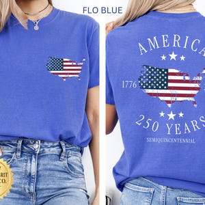 May include: Flo blue t-shirt with a pocket featuring an American flag map. The back of the shirt displays "AMERICA" above a flag map, "1776-2026", and "250 YEARS SEMIQUINCENTENNIAL".