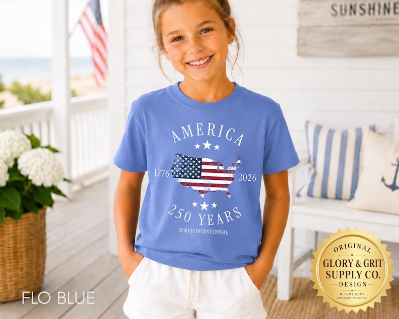 May include: A Flo Blue t-shirt with the word "AMERICA" and the years "1776" and "2026" printed on it. The shirt features a map of the United States with the American flag design. The text "250 YEARS SEMIQUINCENTENNIAL" is also printed on the shirt.