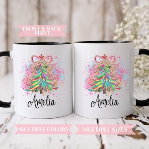 May include: Two white mugs with black handles and rims. Each mug features a colorful Christmas tree design with the name "Amelia" below. The text "FRONT & BACK PRINT", "MULTIPLE COLORS", and "MULTIPLE SIZES" are also visible.