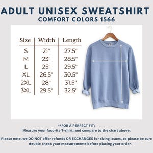 May include: A light blue unisex sweatshirt hanging on a wooden hanger. The image includes a size chart with measurements in inches for width and length, ranging from size small to 3XL. Text at the top reads "ADULT UNISEX SWEATSHIRT COMFORT COLORS 1566."