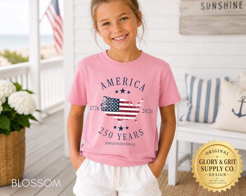 May include: A pink t-shirt with the word "AMERICA" above a map of the United States with the American flag inside. The shirt also has the text "1776 2026 250 YEARS SEMIQUINCENTENNIAL". The shirt is worn by a young person.