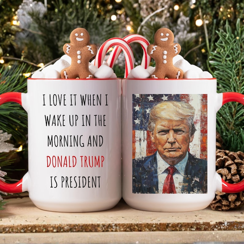 K&ouml;nnte beinhalten: Zwei wei&szlig;e Keramikbecher mit roten Griffen, mit dem Text "I LOVE IT WHEN I WAKE UP IN THE MORNING AND DONALD TRUMP IS PRESIDENT." Ein Becher hat ein Portr&auml;t von Donald Trump. Lebkuchenm&auml;nner und Zuckerstangen schm&uuml;cken die Becher.