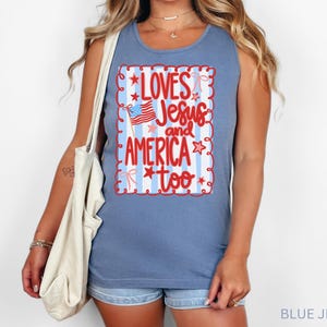 K&ouml;nnte beinhalten: Ein blaues Jeans-Tanktop mit dem Text "Loves Jesus and America too" in einem rot-wei&szlig;en Design. Das Design enth&auml;lt eine kleine amerikanische Flagge und Sterne. Das Tanktop ist &auml;rmellos und hat einen Rundhalsausschnitt.