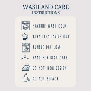 May include: Cream-colored card with navy blue text and icons detailing wash and care instructions. The instructions include machine wash cold, turn item inside out, tumble dry low, hang for best care, do not iron design, and do not bleach.