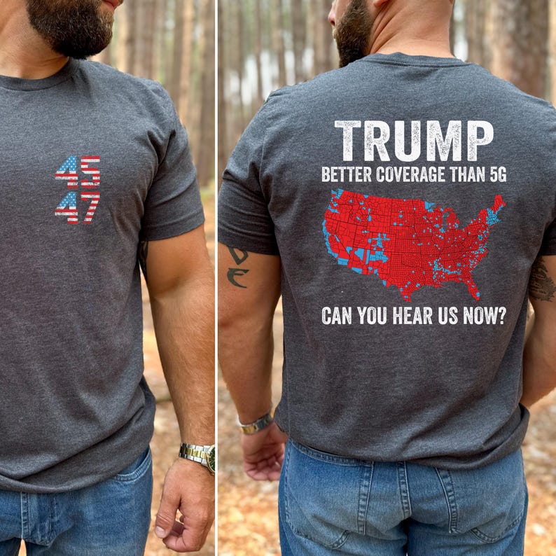 May include: A dark gray t-shirt with a red, white, and blue American flag design on the front and a map of the United States with red and blue markings on the back. The back of the shirt also has the text "TRUMP BETTER COVERAGE THAN 5G CAN YOU HEAR US NOW?"