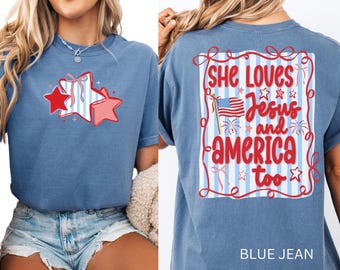 May include: Blue jean-colored t-shirt with a patriotic star graphic on the front. The back of the shirt features the text "She Loves Jesus and America too" with an American flag and fireworks.