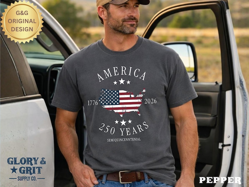 May include: A gray t-shirt with the word "AMERICA" above a map of the United States with the American flag design. The shirt also features the text "1776" and "2026" and "250 YEARS". The shirt is a "G&G ORIGINAL DESIGN" from "GLORY & GRIT SUPPLY CO."