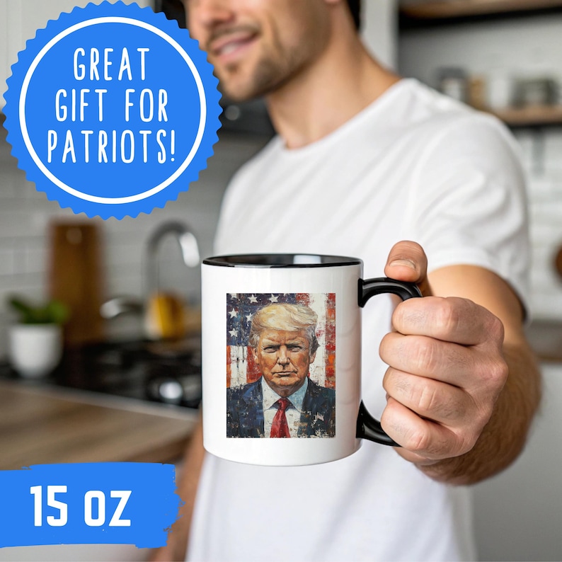 K&ouml;nnte beinhalten: Eine wei&szlig;e Keramik-Tasse mit schwarzem Innenraum und Griff, die ein Portr&auml;t eines Mannes vor dem Hintergrund der amerikanischen Flagge zeigt. Die Tasse ist mit "15 OZ" beschriftet und hat eine blaue Grafik mit "GREAT GIFT FOR PATRIOTS!"