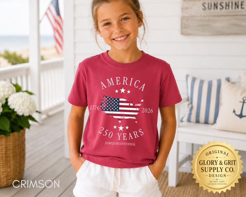 May include: A crimson t-shirt with the word "AMERICA" above a map of the United States with the American flag inside. The text "250 YEARS SEMIQUINCENTENNIAL" is below the map. The shirt is worn by a young person.