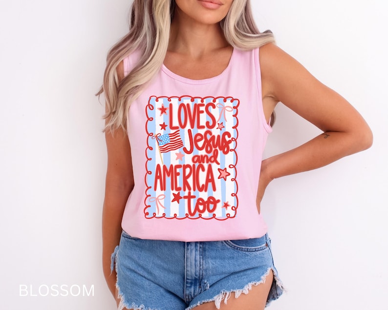 K&ouml;nnte beinhalten: Ein hellrosa Tanktop mit dem Schriftzug "LOVES Jesus and AMERICA too" in roter Schrift. Das Design beinhaltet eine amerikanische Flagge und ist von einem dekorativen Rahmen mit Sternen und Streifen umgeben.