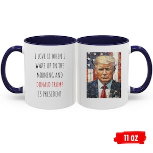 K&ouml;nnte beinhalten: Wei&szlig;er Keramikbecher mit marineblauem Innenraum und Griff. Der Becher zeigt den Text "I LOVE IT WHEN I WAKE UP IN THE MORNING AND DONALD TRUMP IS PRESIDENT" und ein Portr&auml;t von Donald Trump. Fassungsverm&ouml;gen: 325 ml.