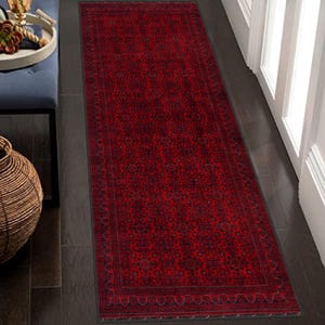May include: A red runner rug with a black and white geometric pattern. The rug has a border with a wavy design.