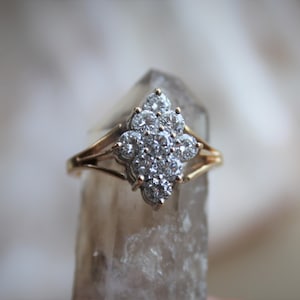 May include: A gold ring with a large cluster of clear diamonds set in a flower-like design.