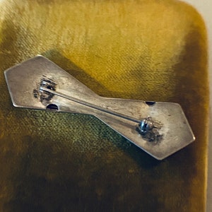 Peut inclure: L'arri&egrave;re d'une broche argent&eacute;e en forme de n&oelig;ud papillon. La broche est munie d'une &eacute;pingle et d'un fermoir.