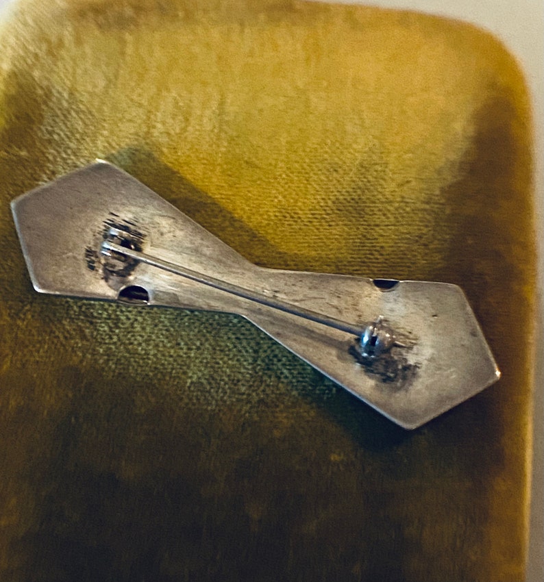 Peut inclure: L'arri&egrave;re d'une broche argent&eacute;e en forme de n&oelig;ud papillon. La broche est munie d'une &eacute;pingle et d'un fermoir.