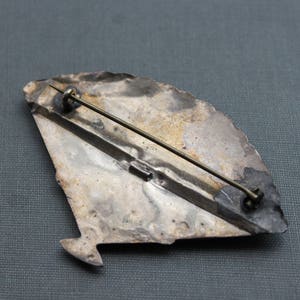May include: Silver tone brooch with a fan-shaped design. The brooch has a pin and catch closure on the back.