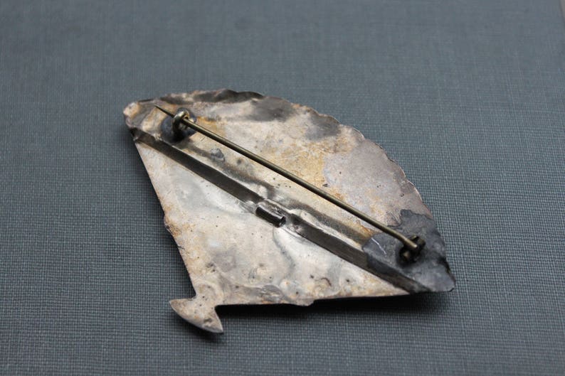 May include: Silver tone brooch with a fan-shaped design. The brooch has a pin and catch closure on the back.