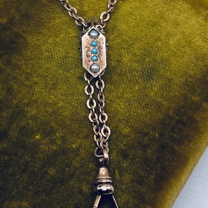 May include: A silver watch chain with a decorative pendant featuring turquoise and pearl accents. The chain has a swivel clasp.