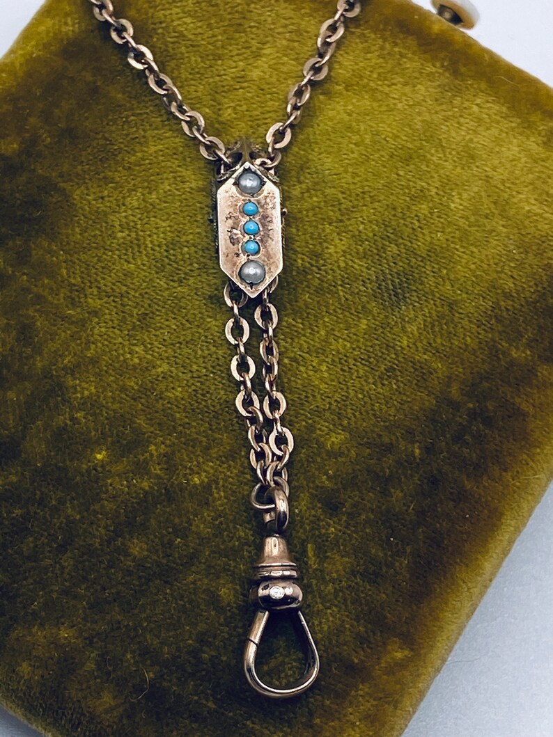 May include: A silver watch chain with a decorative pendant featuring turquoise and pearl accents. The chain has a swivel clasp.