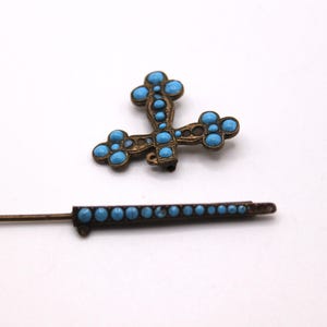 May include: An antique bronze cross pendant and matching pin, both decorated with turquoise-coloured stones. The cross has a detailed design, while the pin has a row of stones. A vintage jewellery set.