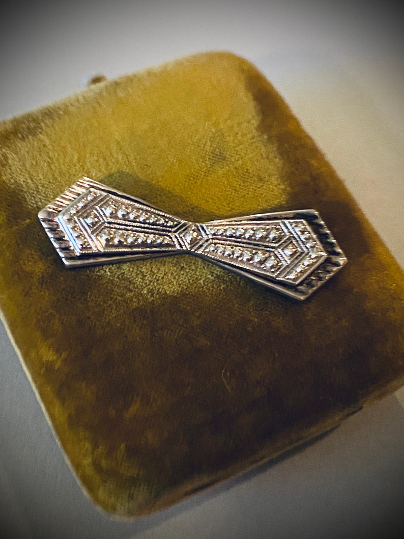 Peut inclure: Une broche en forme de n&oelig;ud en argent avec un motif g&eacute;om&eacute;trique, plac&eacute;e dans un &eacute;crin en velours.