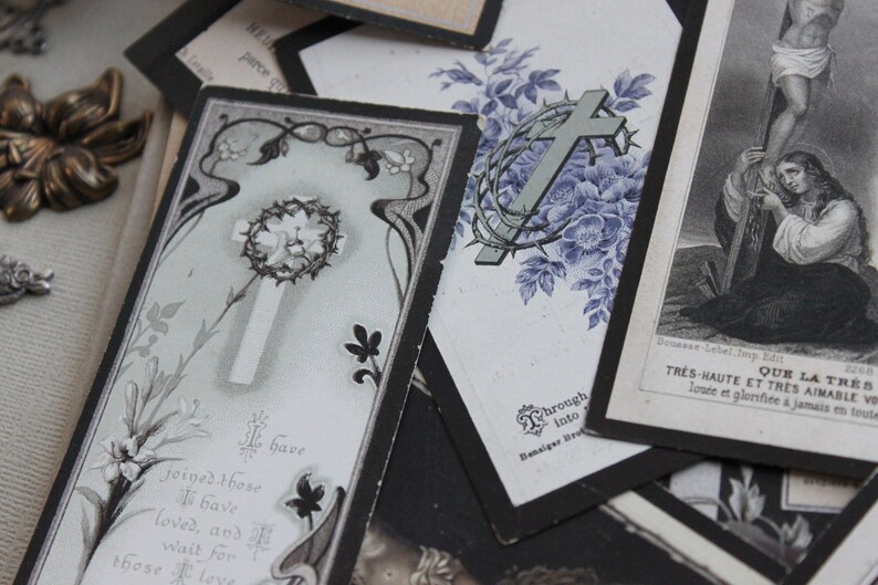 May include: A collection of vintage religious cards with black borders and floral designs. The cards feature crosses, thorns, and religious text in French. The text reads "Que la tres haute et tres aimable vous louee et glorifiee a jamais en tout"