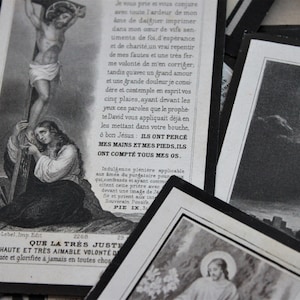 May include: Two vintage religious cards with black borders. The first card features a black and white illustration of Jesus on the cross. The second card features a black and white illustration of a woman kneeling in prayer. The text on the second card reads "Que la tres juste tres haute et tres aimable volont&eacute; de lou&eacute;e et glorifi&eacute;e &agrave; jamais en toutes choses".
