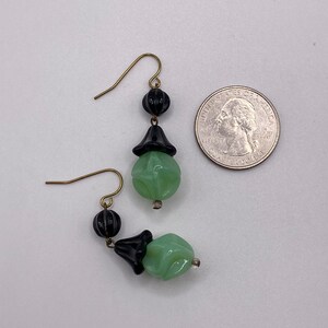May include: A pair of dangle earrings with green and black glass beads. The earrings have a gold-tone hook and are approximately the size of a quarter.