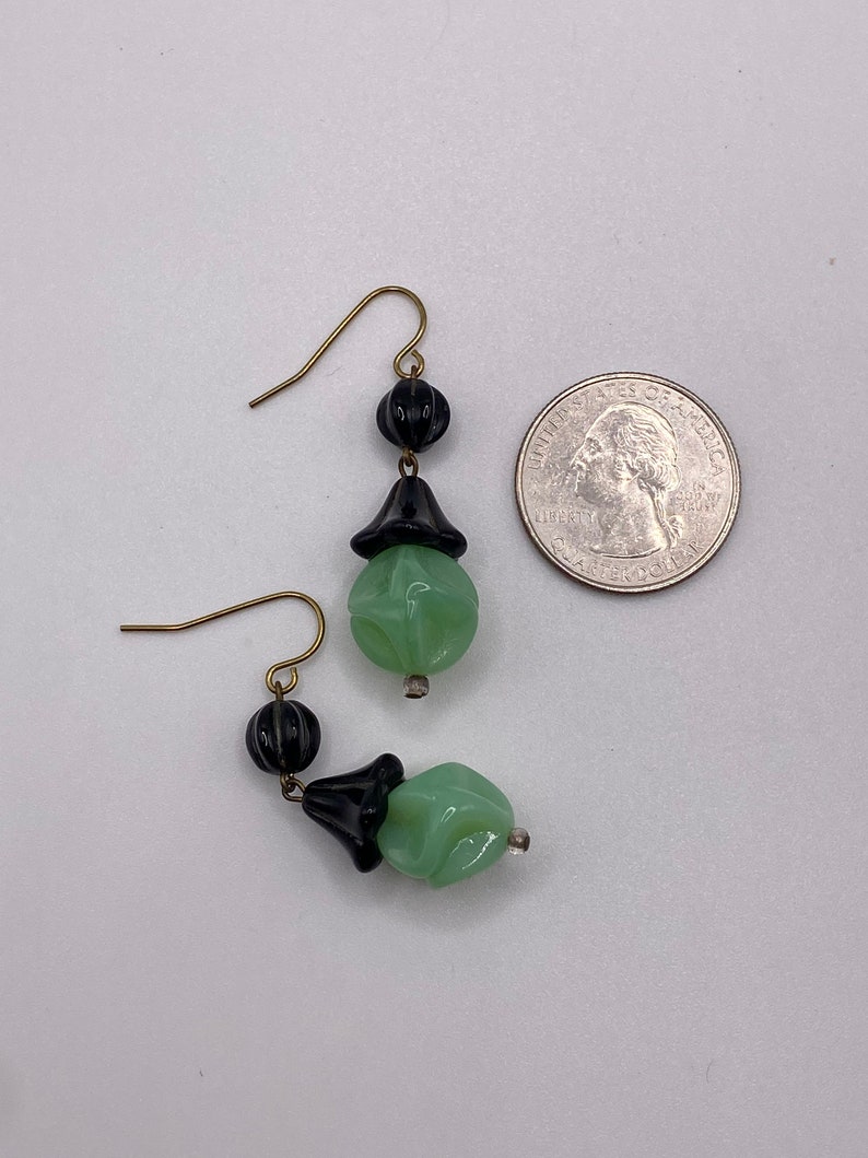 May include: A pair of dangle earrings with green and black glass beads. The earrings have a gold-tone hook and are approximately the size of a quarter.