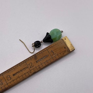 May include: A pair of dangle earrings with a green and black glass bead and a black metal flower charm. The earrings are approximately 2 inches long.