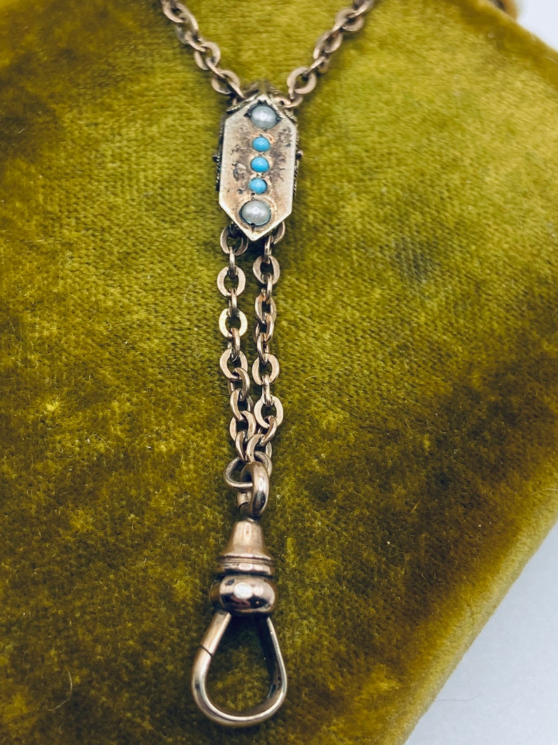 May include: A silver pocket watch chain with a decorative fob featuring turquoise and pearl accents. The chain has a swivel clasp.