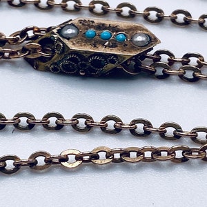 May include: A gold chain necklace with a decorative pendant. The pendant is rectangular in shape with a textured surface and features small blue and white stones.