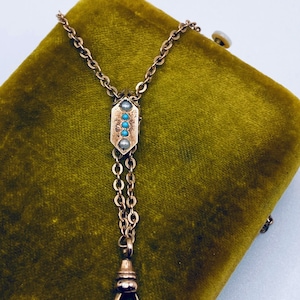 May include: A gold chain watch fob with a decorative pendant featuring turquoise and pearl accents. The fob is on a green velvet background.