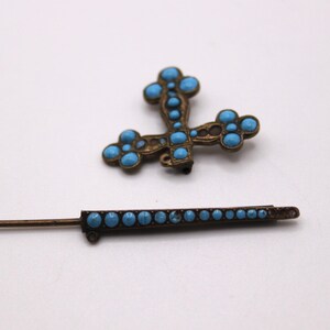 May include: An antique brooch and pin set. The cross-shaped brooch and the pin are both bronze-toned and decorated with turquoise-coloured stones. The cross has rounded edges and the pin is a straight bar with a series of turquoise stones.