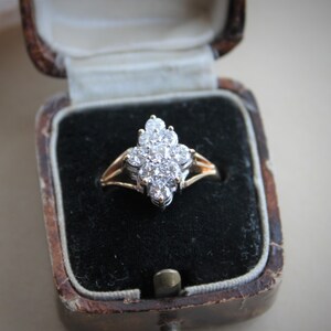 May include: A diamond ring with a cluster of small diamonds set in a gold band. The ring is displayed in a black velvet ring box.