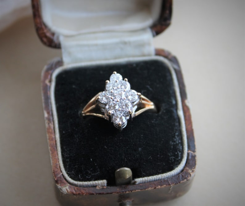 May include: A diamond ring with a cluster of small diamonds set in a gold band. The ring is displayed in a black velvet ring box.