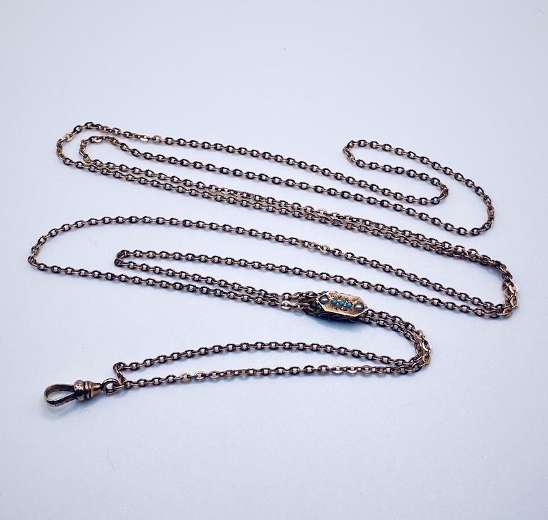 May include: A gold chain necklace with a small, rectangular pendant set with turquoise stones.